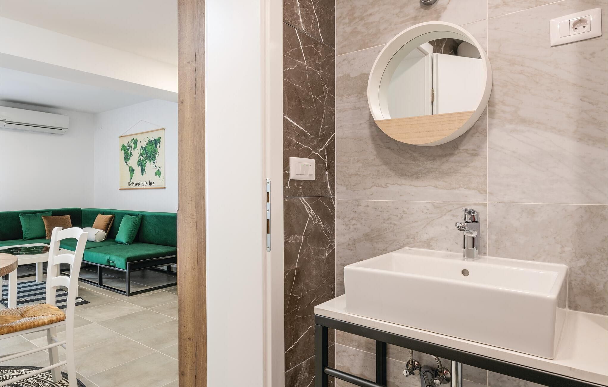 Een moderne badkamer met een witte wastafel, een ronde spiegel en een marmeren achterwand.