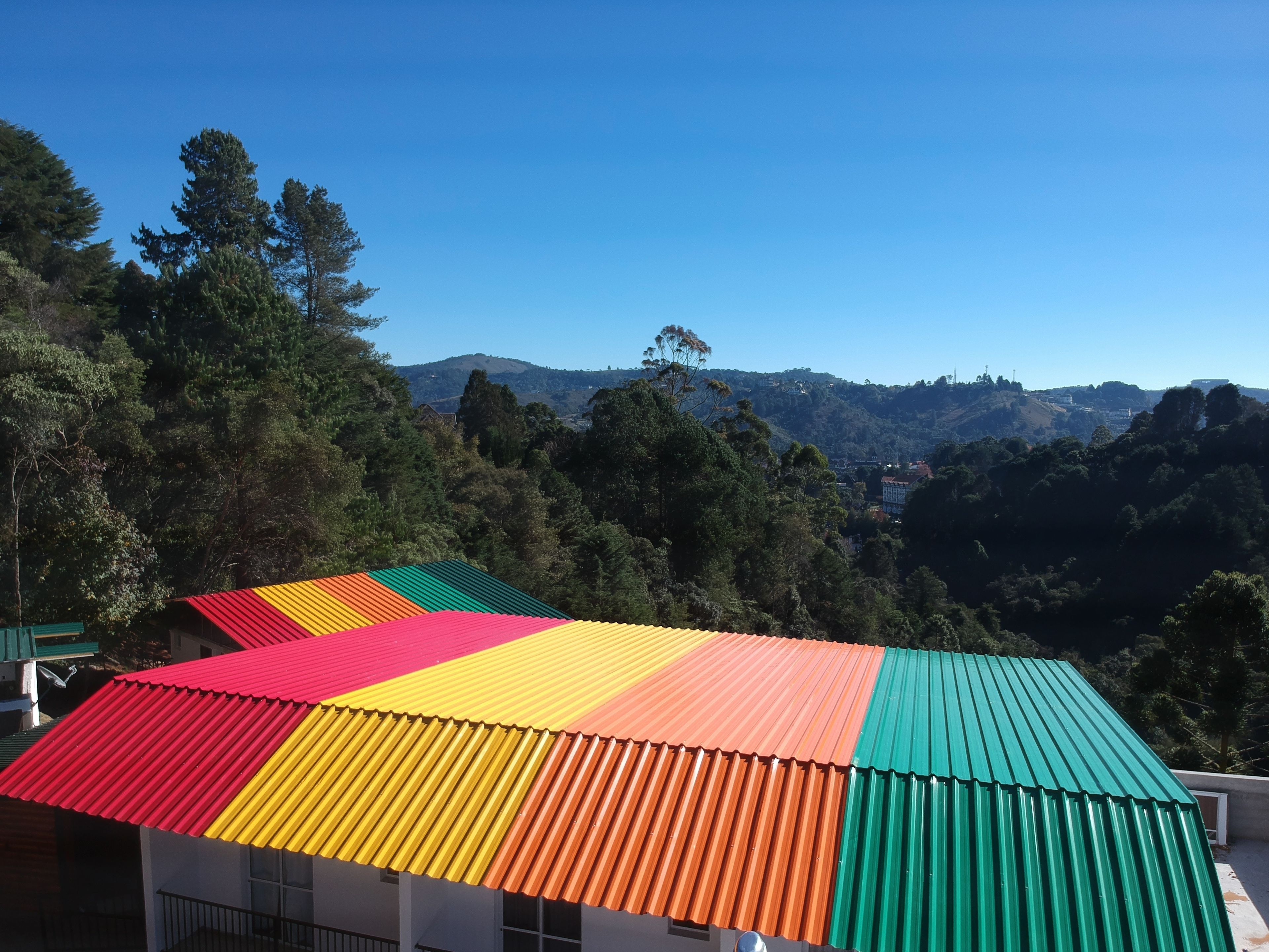 A building with a colorful roof, surrounded by trees and hills.