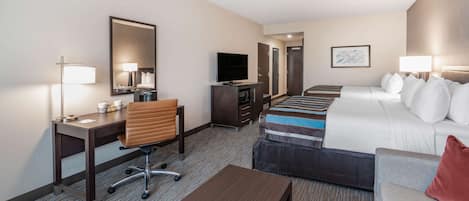 A hotel room with a bed, a desk with a chair, a television, a dresser, and a sofa.