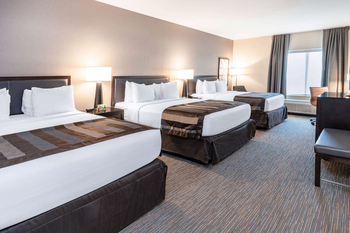 Ein Hotelzimmer mit drei Betten, einem Schreibtisch und zwei Lampen.
