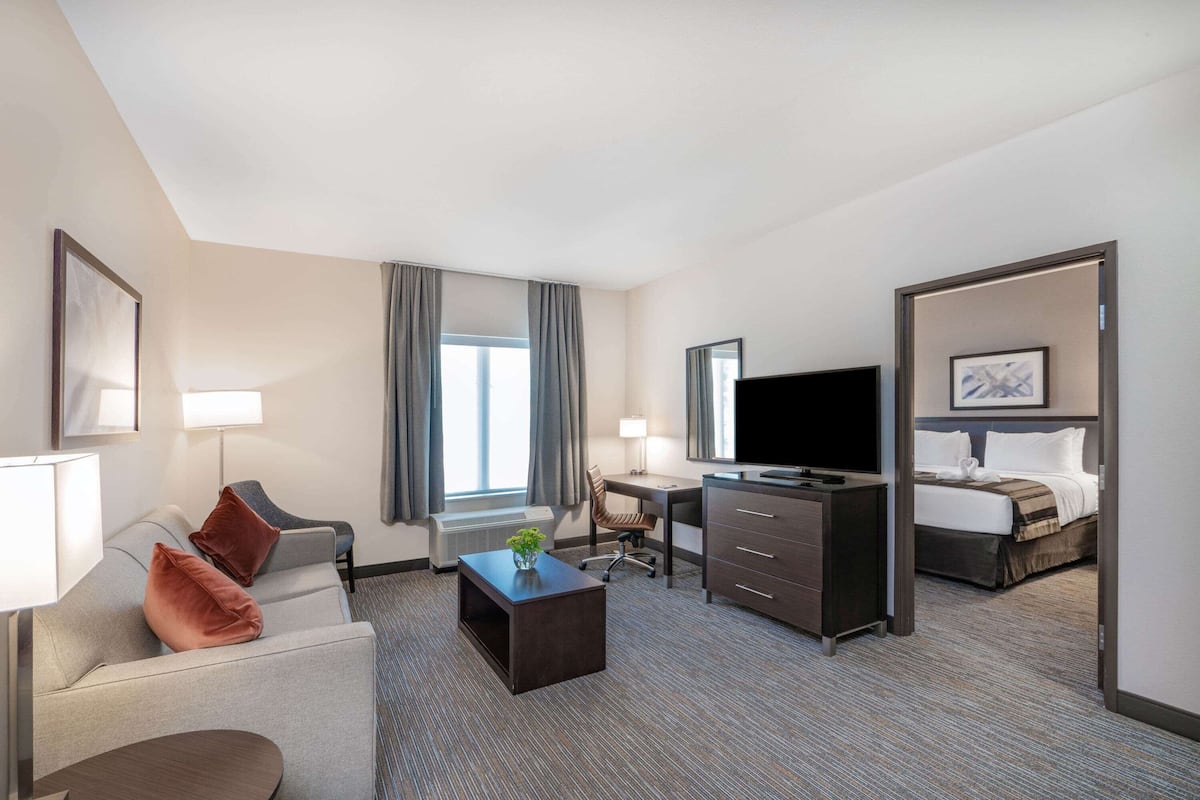 Ein Hotelzimmer mit Sofa, Schreibtisch, Fernseher, Bett und einem Fenster mit Vorhängen.