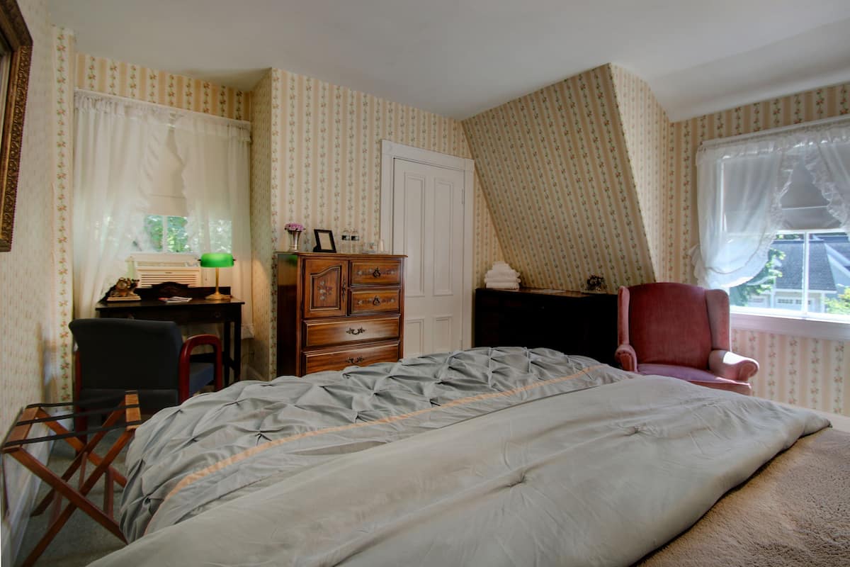 A bedroom with a bed, a desk, a chair, a dresser, and a window with curtains.
