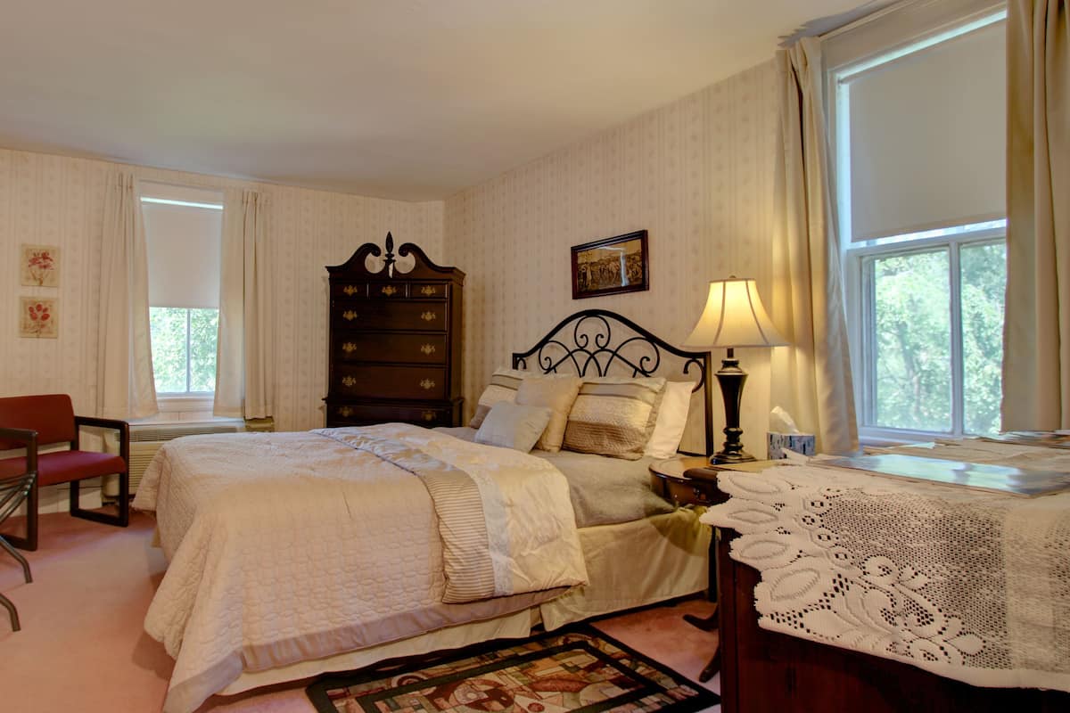 A bedroom with a bed, a chair, a nightstand, a lamp, and a window.