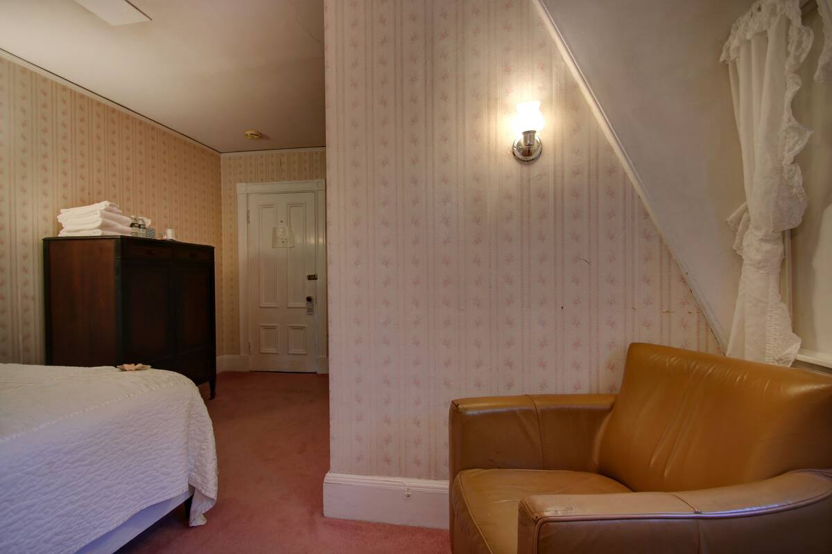 A bedroom with a bed, a chair, a dresser, and a door.