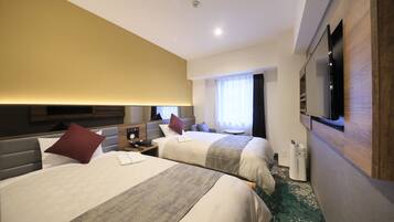 A hotel room with two beds, a television mounted on the wall, a bedside table with a lamp, and a window with curtains.