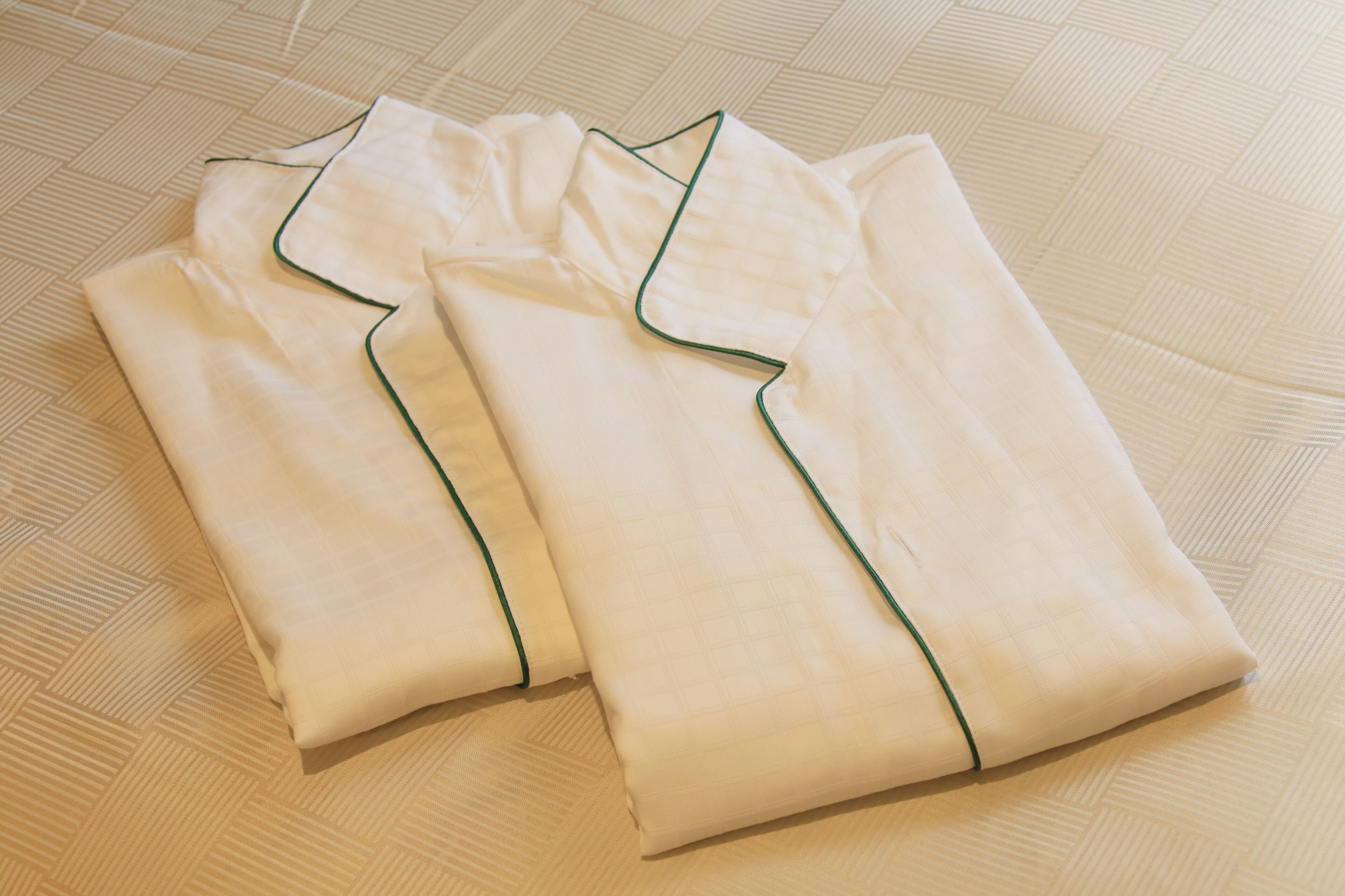 Du linge de lit blanc, soigneusement plié, avec une bordure verte, posé sur un sol beige à texture.