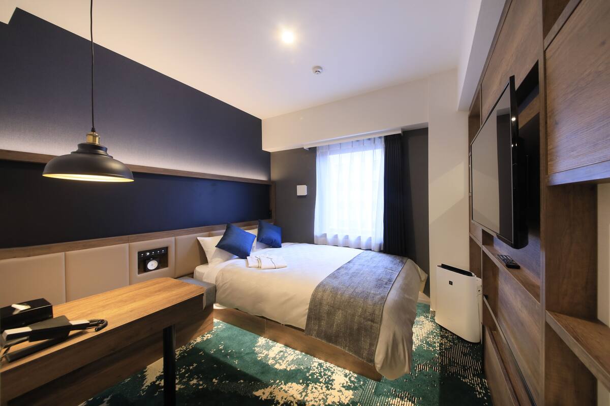 Ein modernes Hotelzimmer mit einem großen Bett, Nachttisch, Schreibtisch und einem Flachbildfernseher.