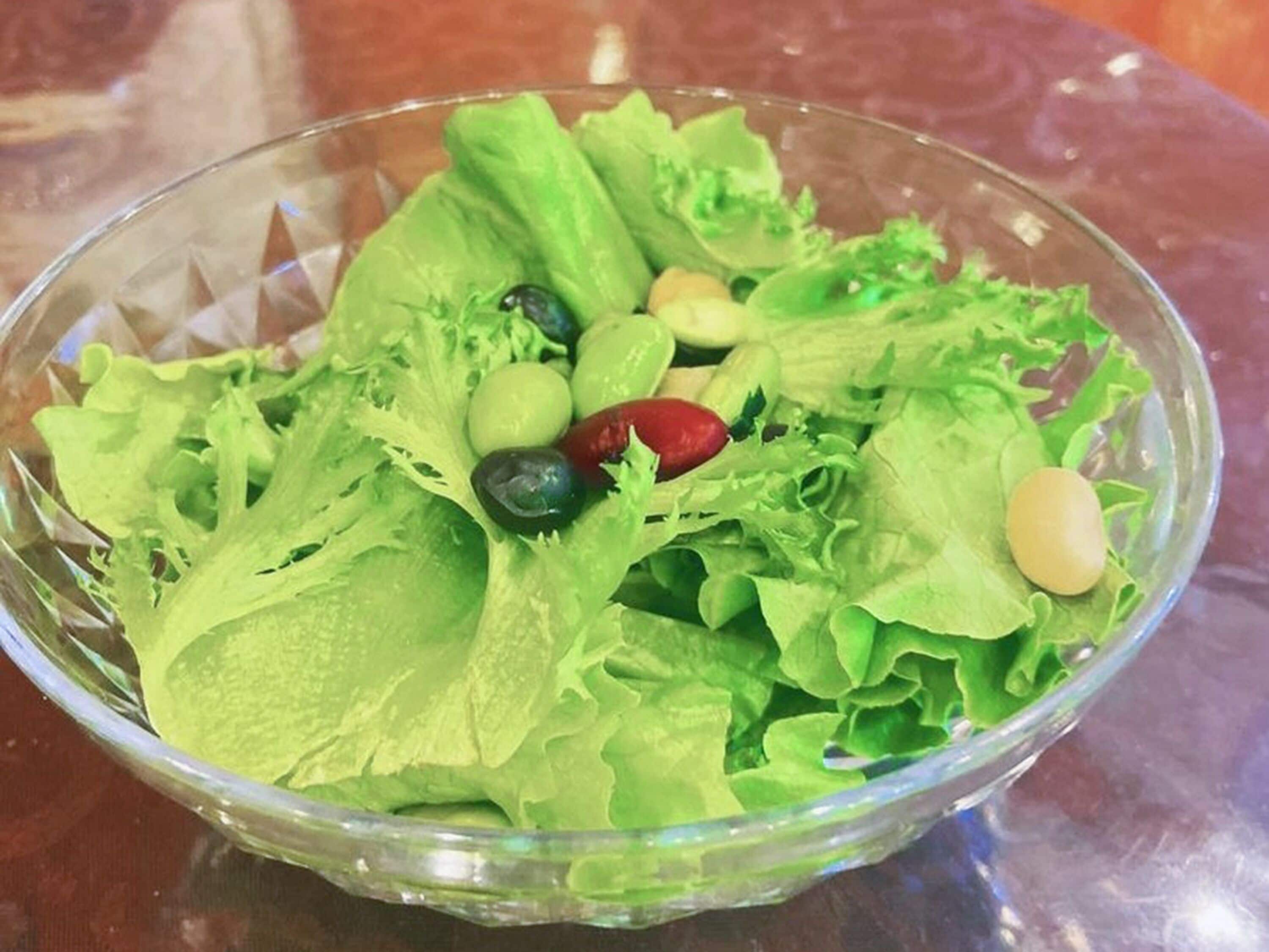 Un saladier en verre transparent contenant une salade composée de laitue, d’olives et d’un poivron rouge.