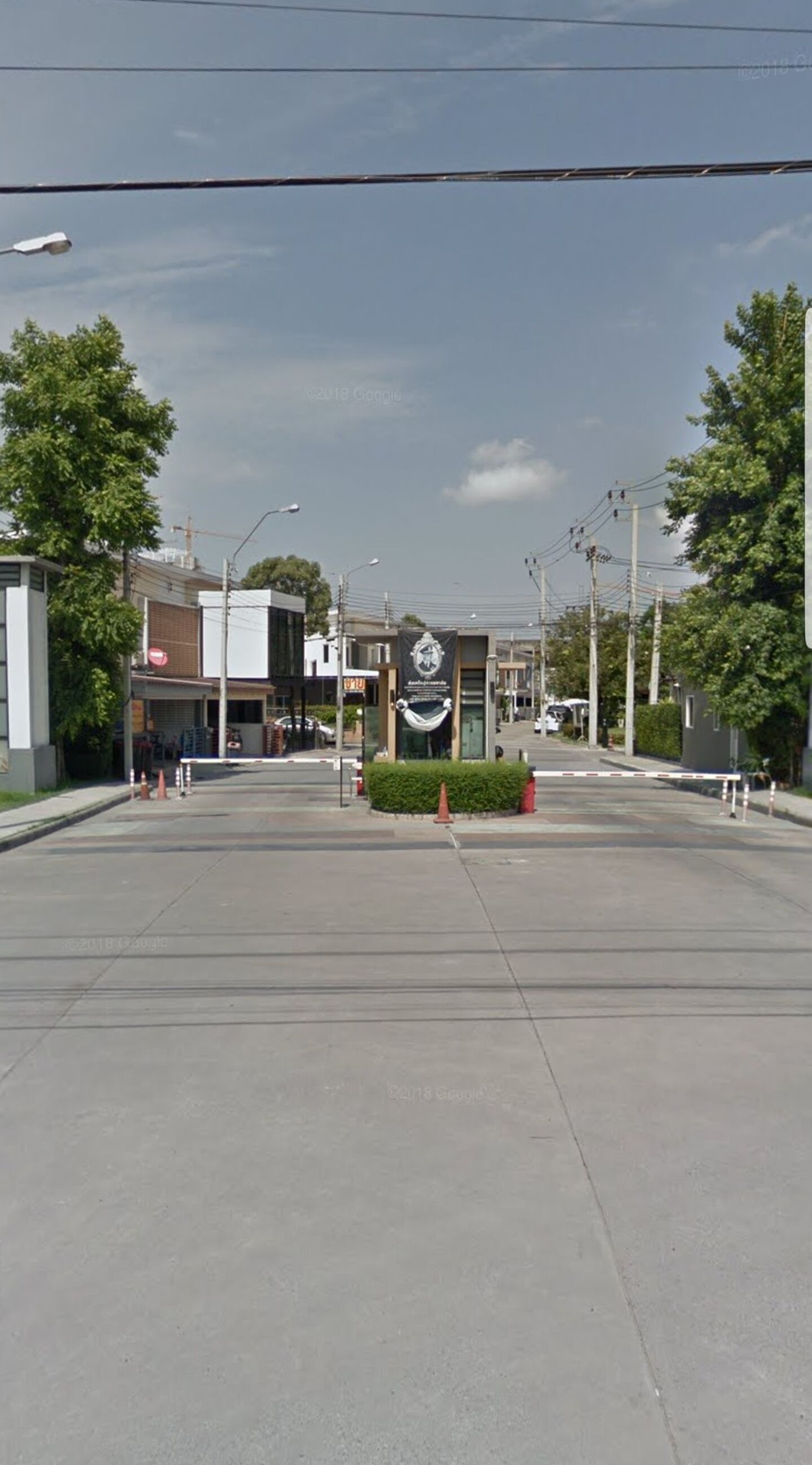 Une large rue bordée de bâtiments des deux côtés, une banderole ornée d’un logo et un ciel d égagé.