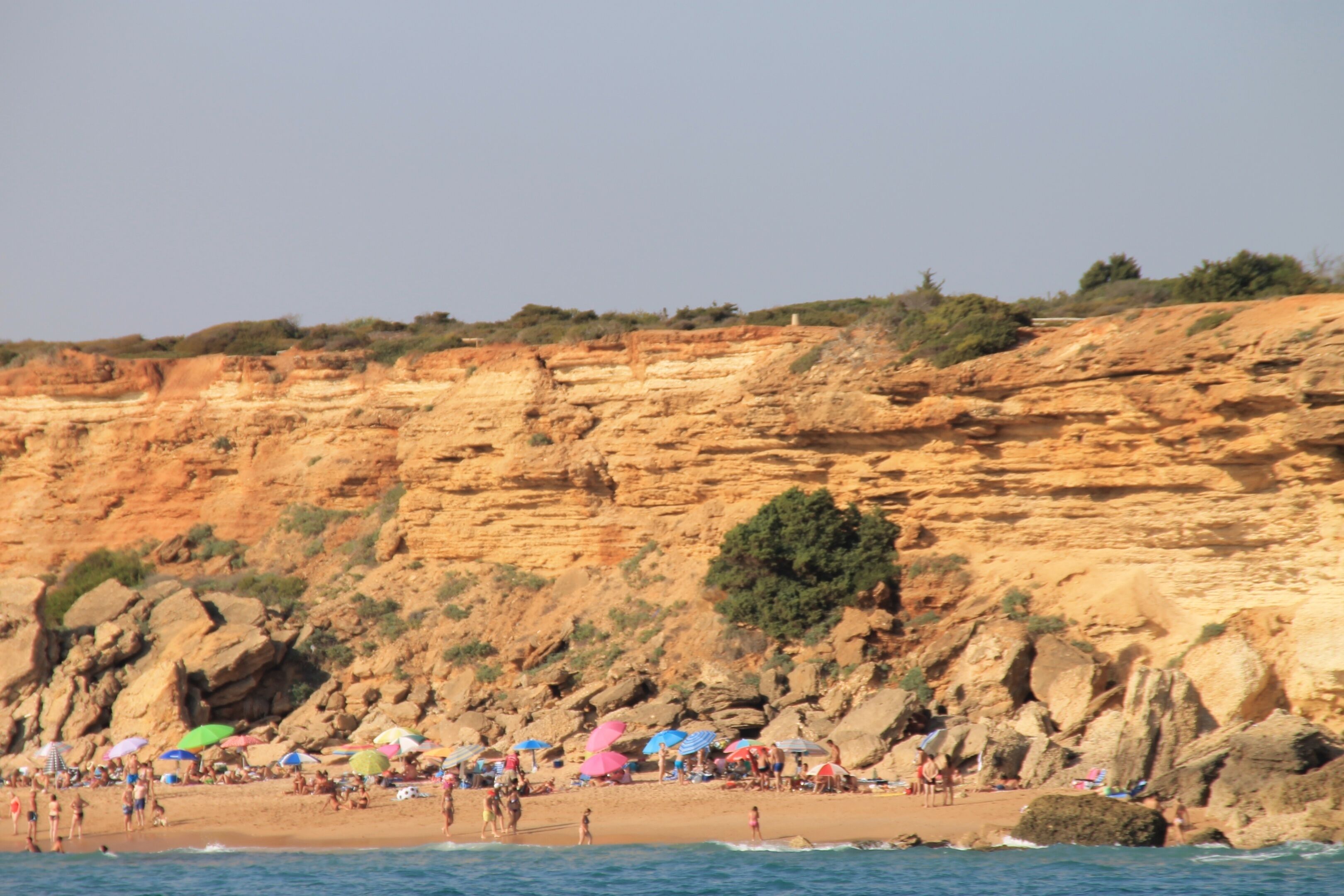 A beach with people, umbrellas, and rocky cliffs.