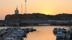 A marina with boats docked, a prominent building with a tower, and a sunset in the background. - Holiday apartment with shared pool (CONIL DE LA FRONTERA)