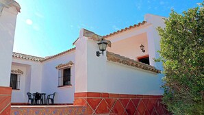 A building with a white facade, red-tiled roof, and a small balcony with a table and chairs. - Holiday apartment with shared pool (CONIL DE LA FRONTERA)