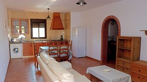 A spacious living room with a sofa, a dining table with chairs, a kitchen area with a washing machine, and a refrigerator. - Holiday apartment with shared pool (CONIL DE LA FRONTERA)