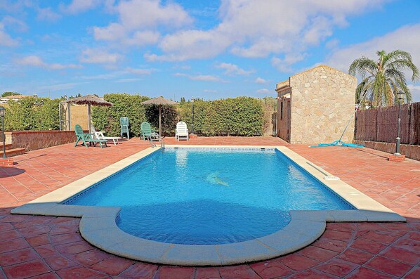 A rectangular swimming pool with a stone wall on one side and a brick patio surrounding it.