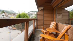 A wooden balcony with two wooden chairs and a table, overlooking a residential area with houses and greenery. - Central village condo w/ hot tub & sauna (Whistler)