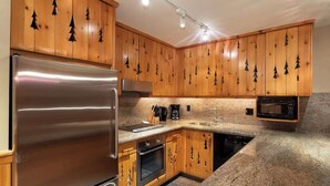 A kitchen with wooden cabinets, a stainless steel refrigerator, a microwave, and granite countertops. - Central village condo w/ hot tub & sauna (Whistler)