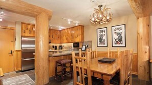 A wooden kitchen with a dining area, featuring a stainless steel refrigerator, wooden cabinets, and a chandelier. - Central village condo w/ hot tub & sauna (Whistler)
