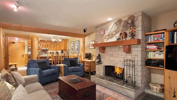 A cozy living room with a stone fireplace, blue sofas, and a wooden coffee table. - Central village condo w/ hot tub & sauna (Whistler)