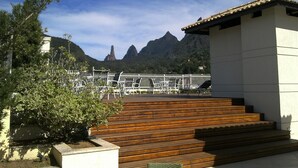 A view of a building with wooden steps leading up to a white structure, surrounded by greenery and mountains in the background. - Style and Comfort - Loft in Alto - Teresópolis - Wifi (Teresópolis)