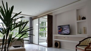 A spacious living room with a large window, a television, and a potted plant. - Style and Comfort - Loft in Alto - Teresópolis - Wifi (Teresópolis)