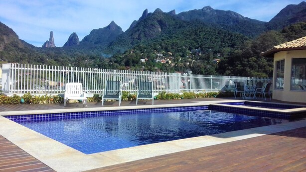 A swimming pool with a wooden deck, surrounded by a white fence, and a mountain backdrop. - Style and Comfort - Loft in Alto - Teresópolis - Wifi (Teresópolis)