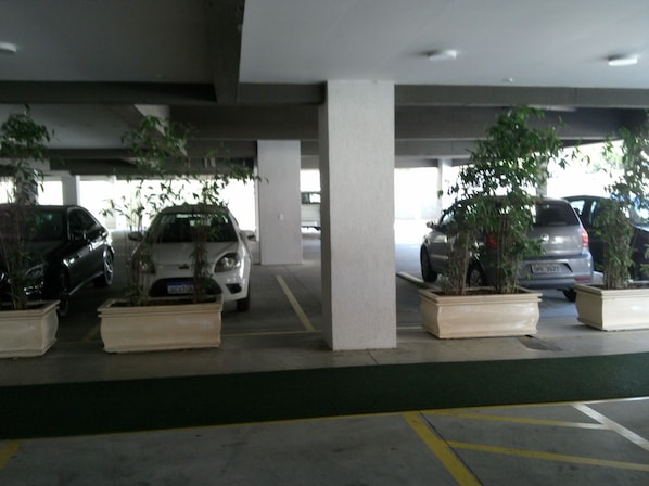 A parking garage with multiple cars parked under concrete pillars, surrounded by potted plants.