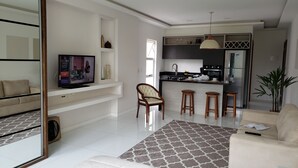 A modern living room with a sofa, a TV, a dining area with stools, and a kitchen with a refrigerator and stove. - Style and Comfort - Loft in Alto - Teresópolis - Wifi (Teresópolis)