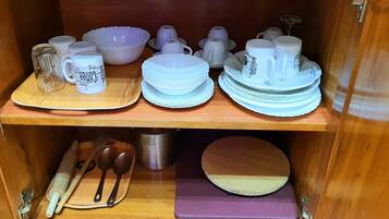 A wooden cabinet with shelves containing white ceramic mugs, plates, bowls, and a metal container.