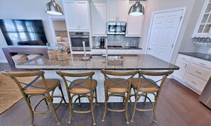 A kitchen with a central island, bar stools, and a dining area with a TV.