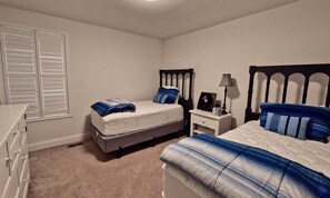 A bedroom with two beds, a nightstand, a dresser, and a window with blinds. - Bayside * 6BR Luxury Beach House (Selbyville)