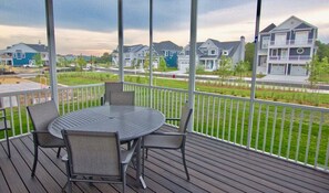 A covered outdoor area with a round table and chairs, a view of residential buildings, and a white fence. - Bayside * 6BR Luxury Beach House (Selbyville)