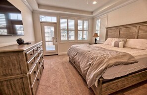 Une chambre à coucher avec un lit, une commode, une lampe et de grandes fenêtres.