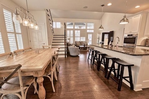 Une cuisine spacieuse avec une table à manger en bois, des tabourets de bar et un escalier menant à un niveau supérieur.