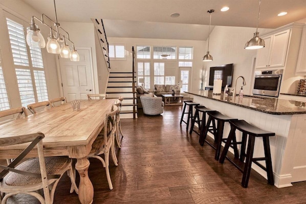 Une cuisine spacieuse avec une table à manger en bois, des tabourets de bar et un escalier menant à un niveau supérieur.