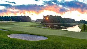 En golfbane med sandbunkere, et vandhazard og en solnedgang i baggrunden.