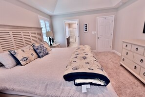 A bedroom with a large bed, a dresser, a nightstand, and a door leading to a bathroom.