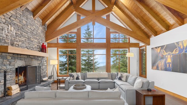 A spacious living room with a stone fireplace, large windows, and a cozy seating area. - Luxury chalet w/ hot tub & media (Whistler)