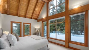 A bedroom with a large bed, wooden beams, and large windows with a snowy view. - Luxury chalet w/ hot tub & media (Whistler)