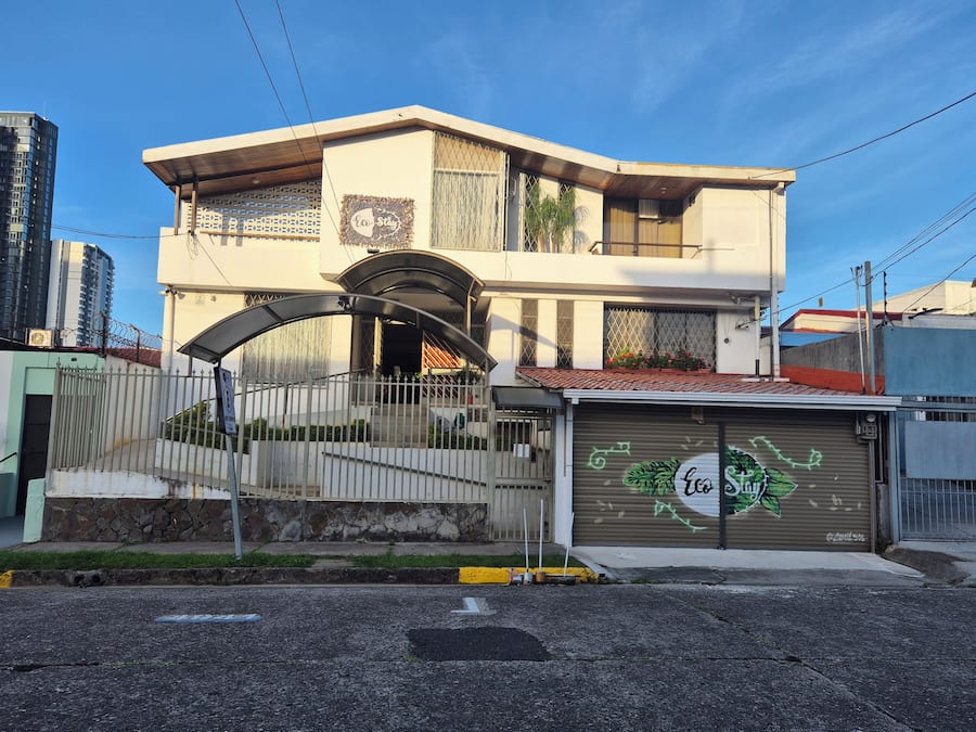 Un bâtiment à deux étages doté d’une entrée sécurisée par un portail, d’un garage à l’esthétique verdoyante et surplombant un ciel dégagé.