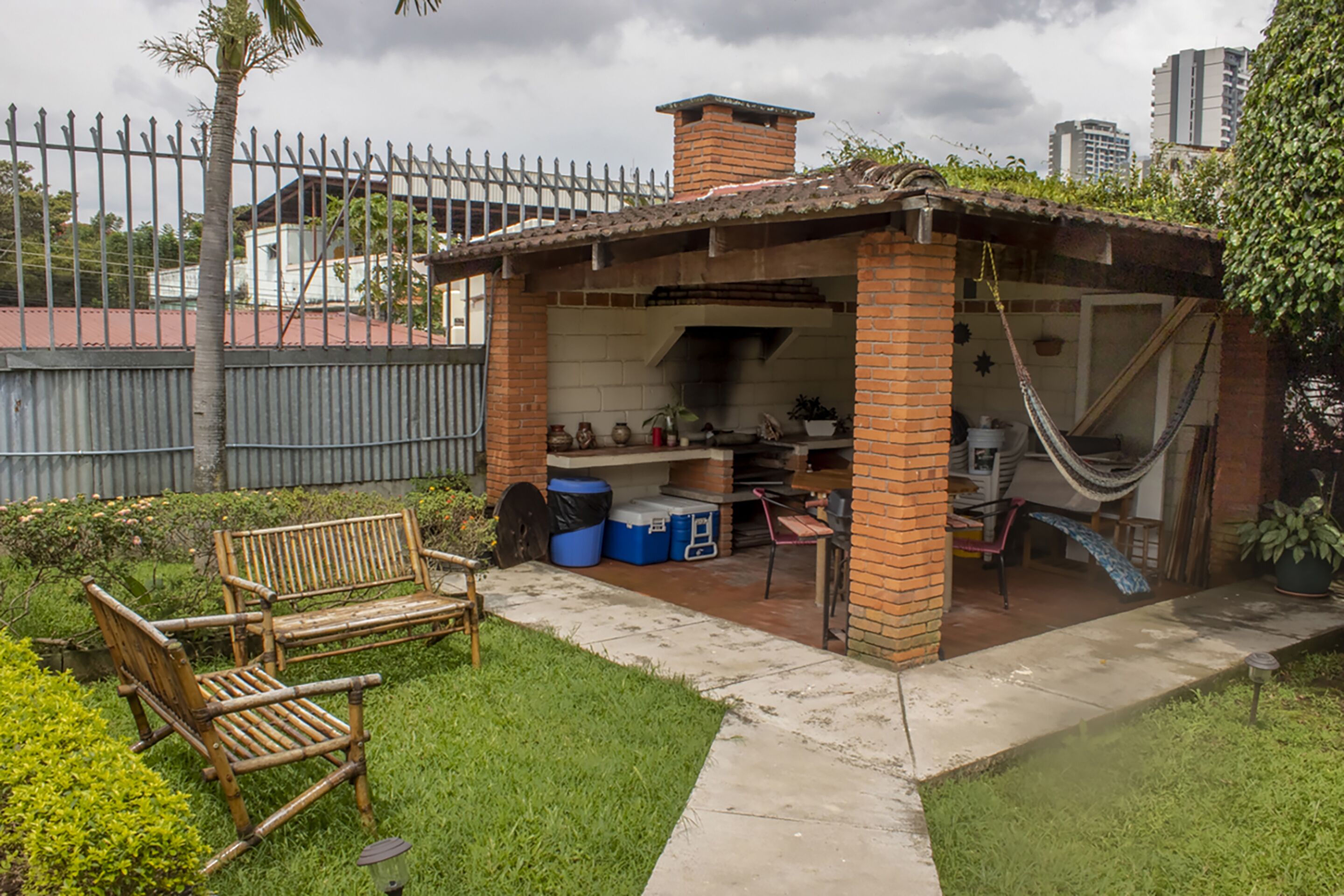 Un jardin avec un espace barbecue en briques, un hamac et un banc en bois.