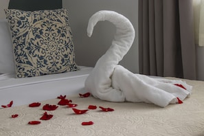 A bed with a swan-shaped towel and red rose petals on a textured white bedspread. - Eco Stay CR (San José)