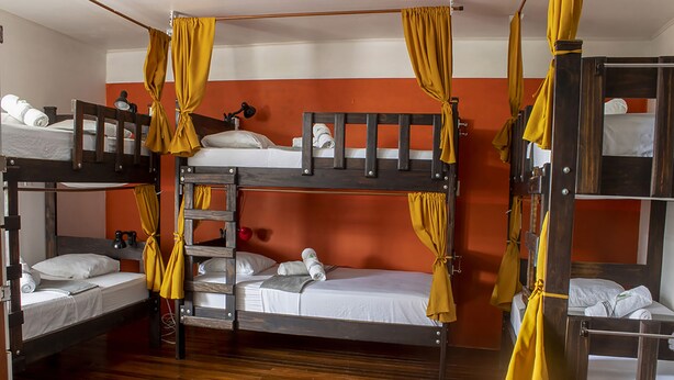 A dormitory room with bunk beds, wooden flooring, and yellow curtains. - Eco Stay CR (San José)