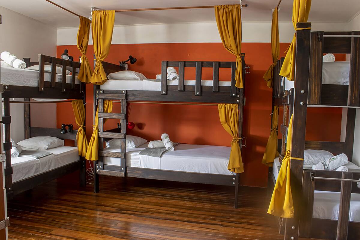 A dormitory room with bunk beds, wooden flooring, and yellow curtains.