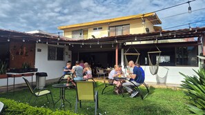 An outdoor seating area with tables and chairs, surrounded by greenery and a building with a yellow facade. - Eco Stay CR (San José)