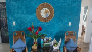 A room with two wicker chairs, a glass table with magazines, a vase with flowers, and a wall with a circular mirror and artwork. - Eco Stay CR (San José)