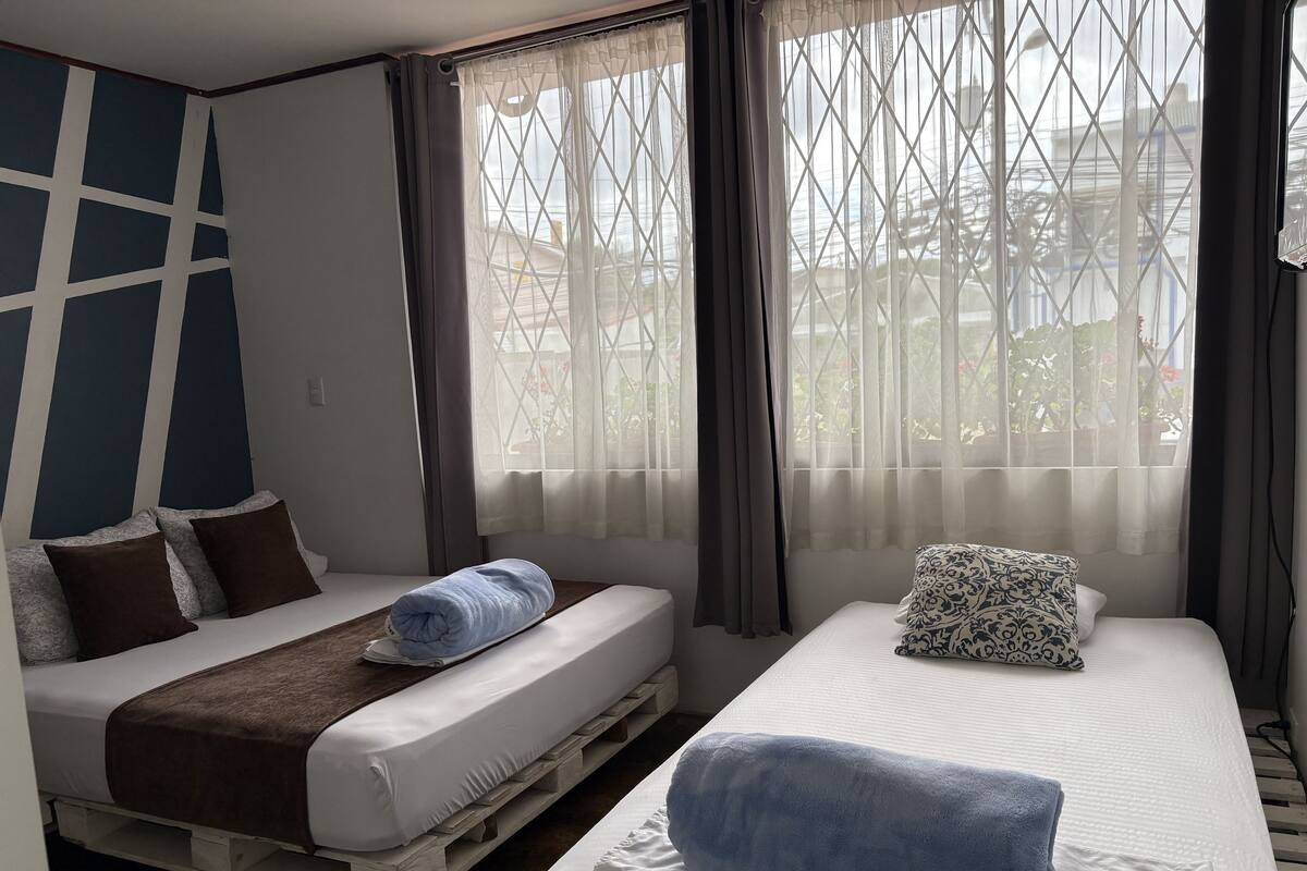 A bedroom with two beds, a window with curtains, and a view of the outside.