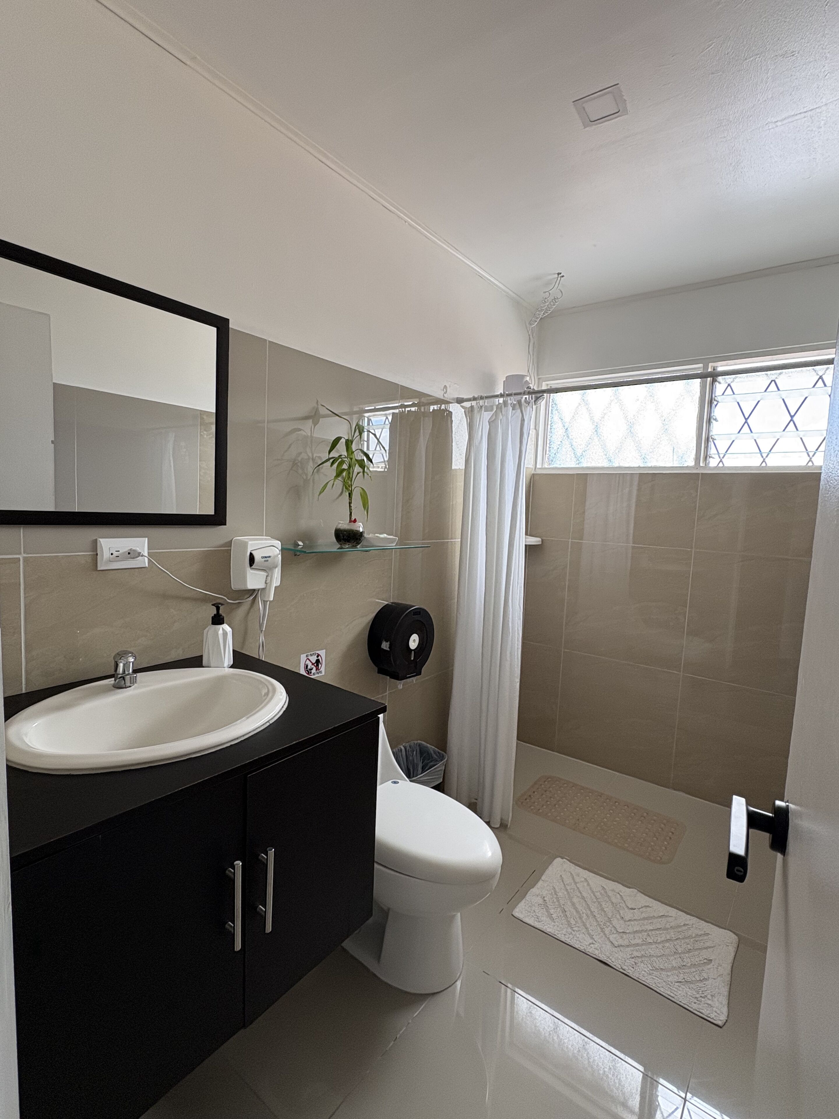 A modern bathroom with a large sink, mirror, and toilet. There is a shower area with a glass door and a towel rack.