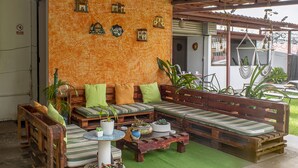 A cozy outdoor seating area with a wooden bench and cushions, surrounded by potted plants and a small table with decorative items. - Eco Stay CR (San José)