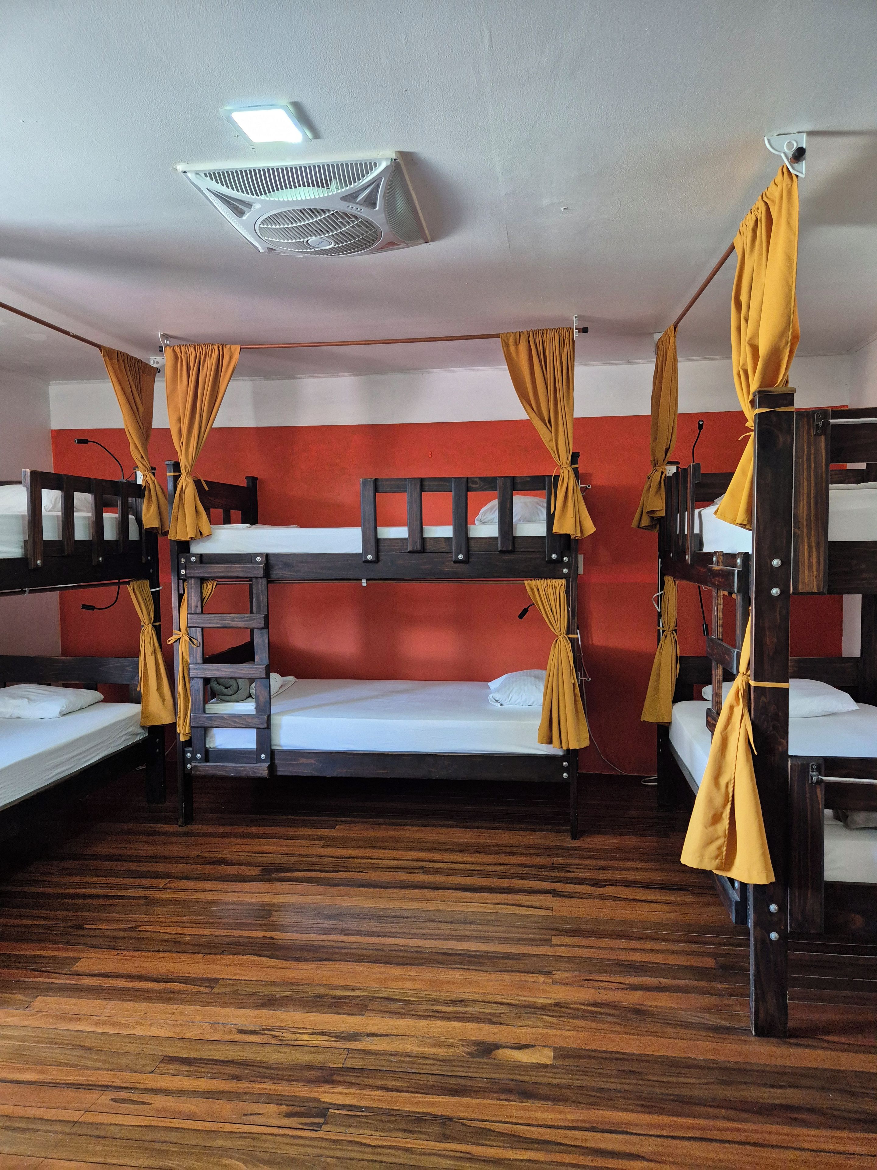A dormitory room with bunk beds, wooden flooring, and a ceiling fan.