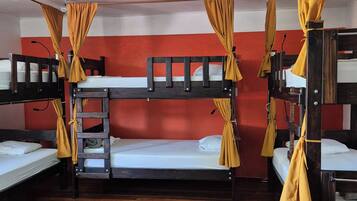 A dormitory room with bunk beds, wooden flooring, and a ceiling fan.